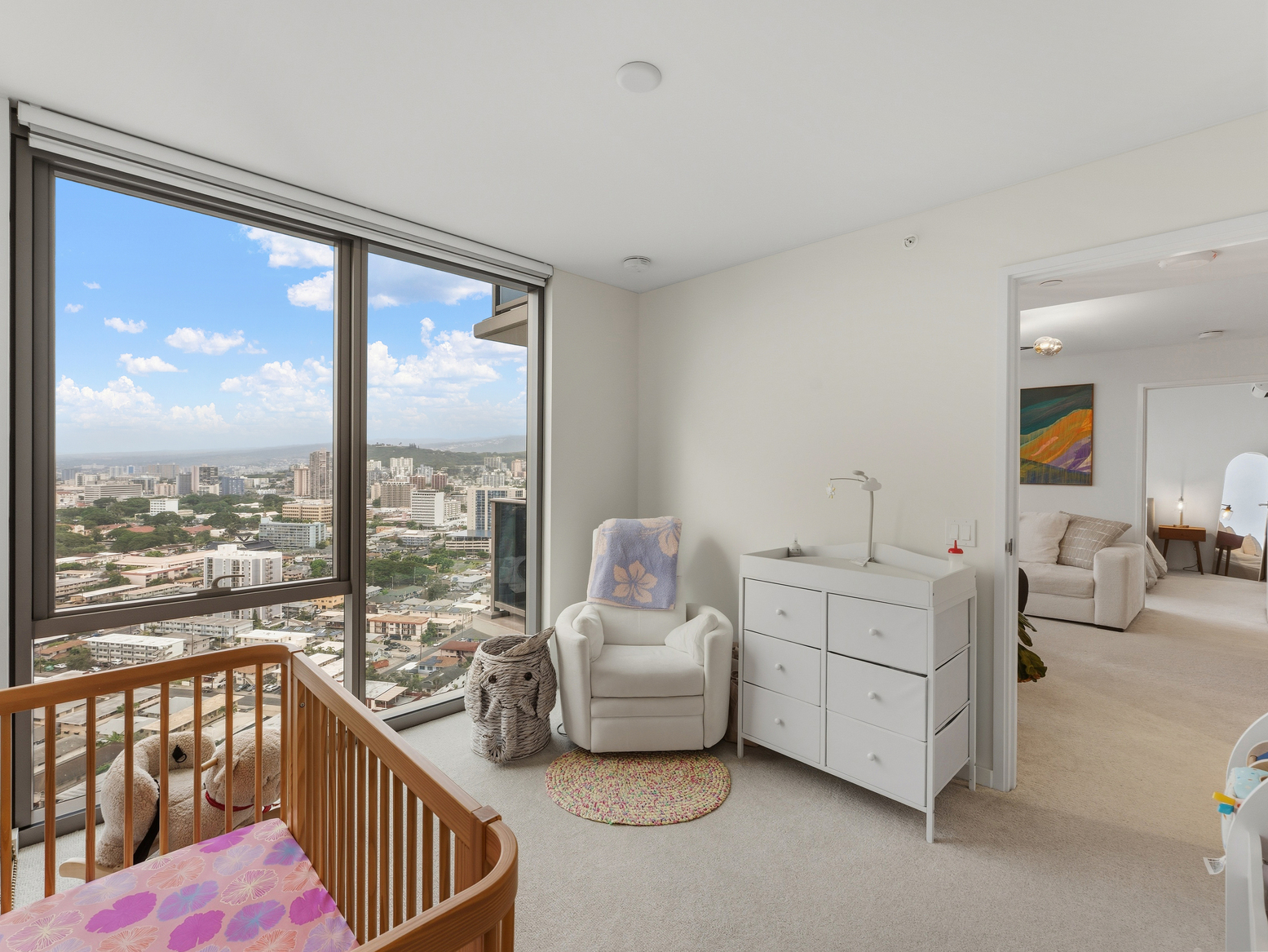 Nursery with crib, glider chair, and changing table beside window city views